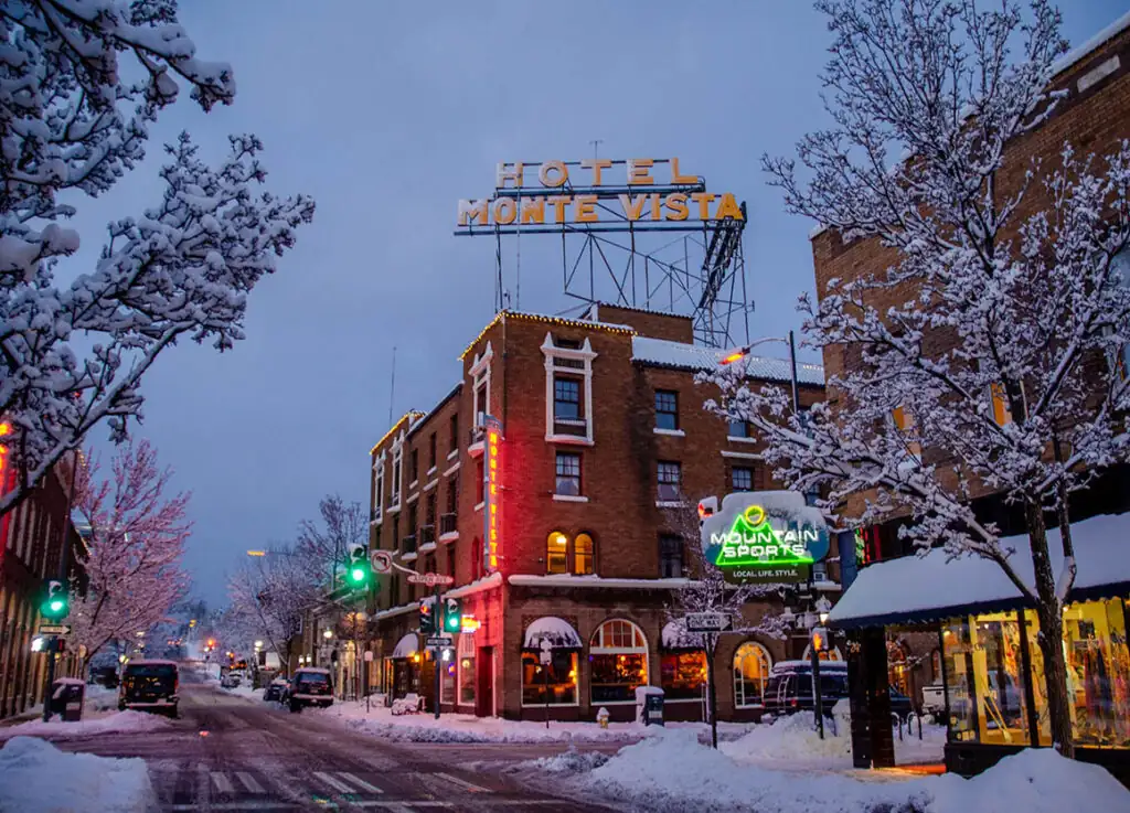 Downtown Flagstaff under fresh snow at dusk, the Hotel Monte Vista sign lit above a snowy street