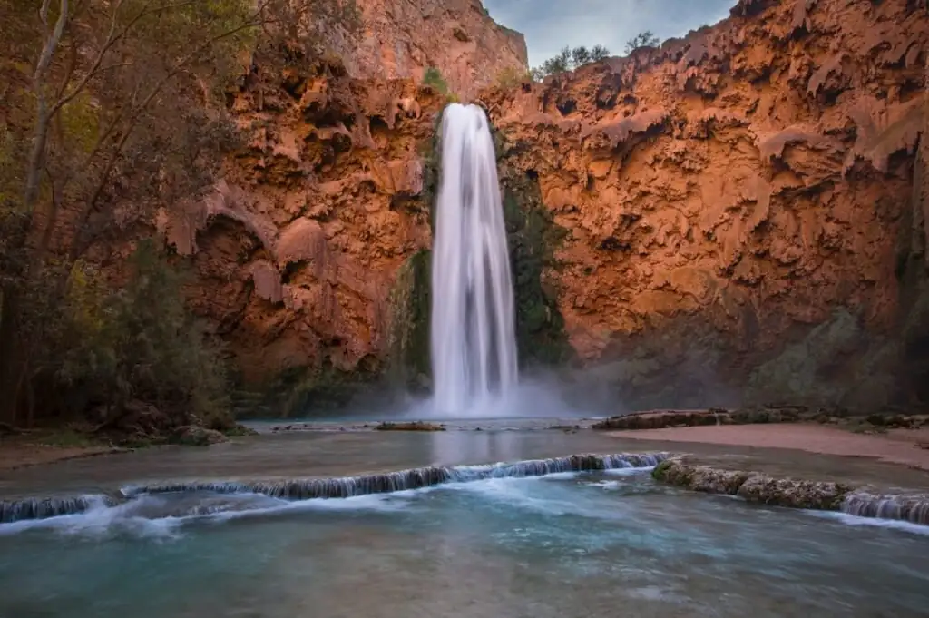 Mooney Falls dropping in a single white column into its pool at dusk