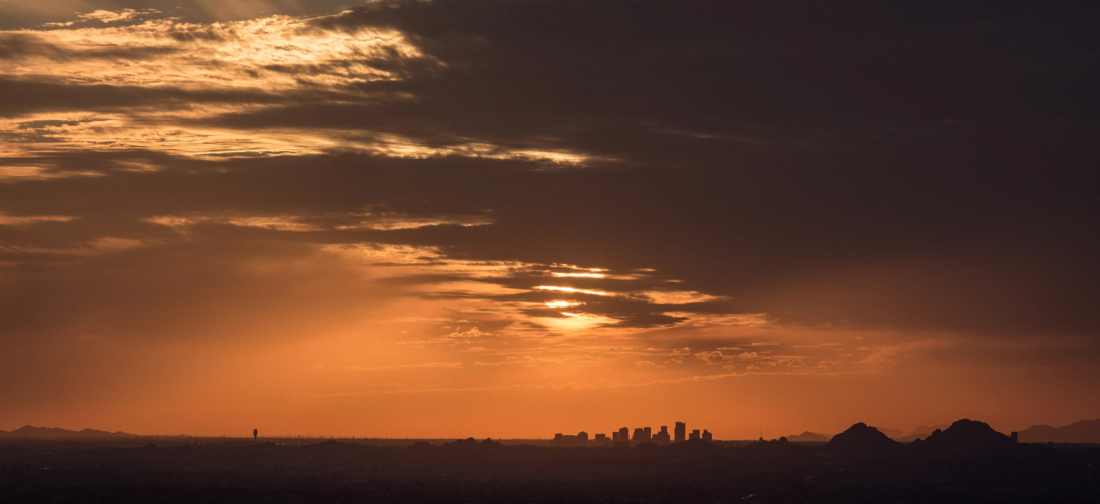 Downtown Phoenix skyline silhouetted under an orange sunset sky