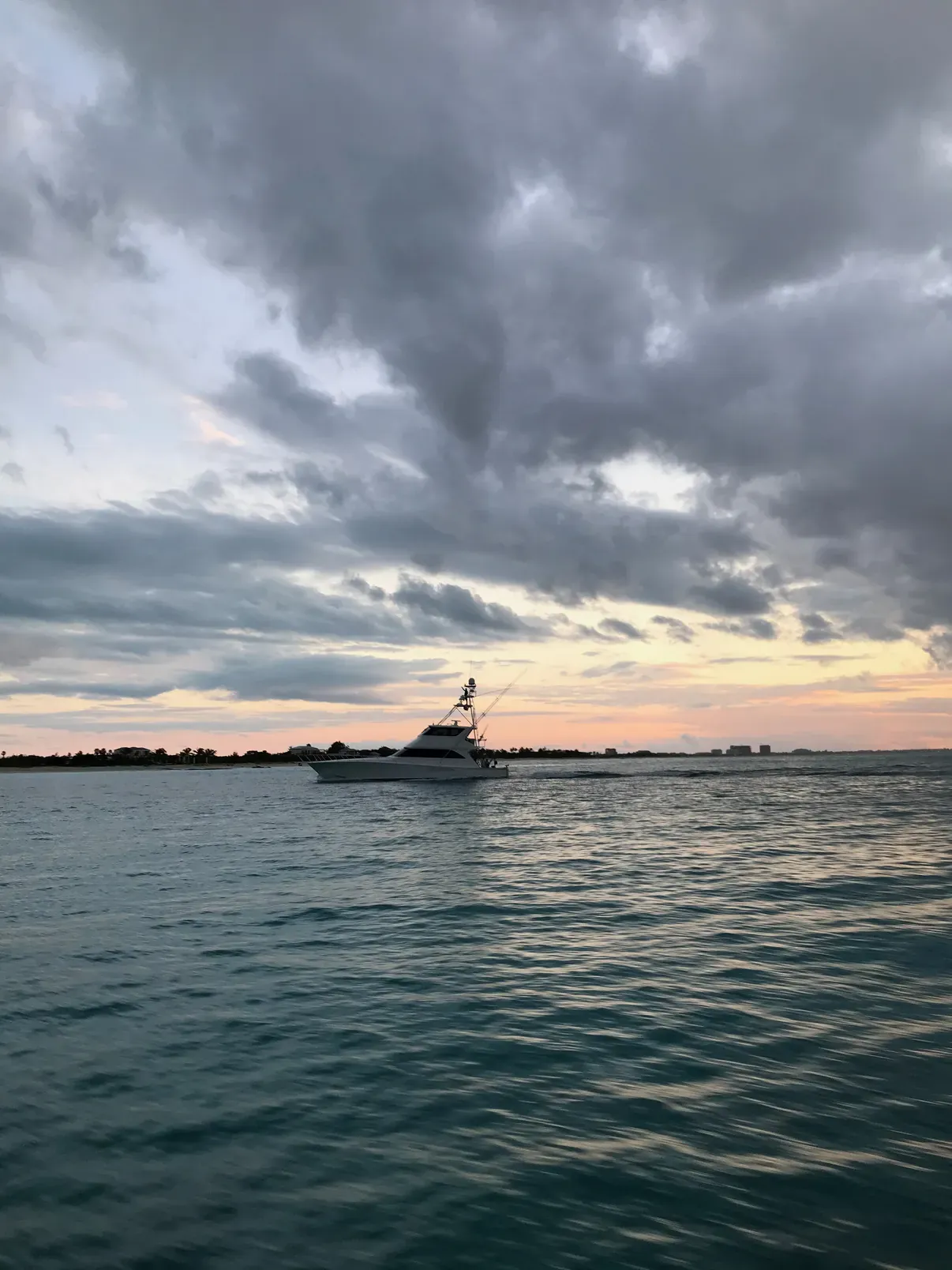 A boat on the horizon at sunset, under heavy dramatic clouds with a band of orange light