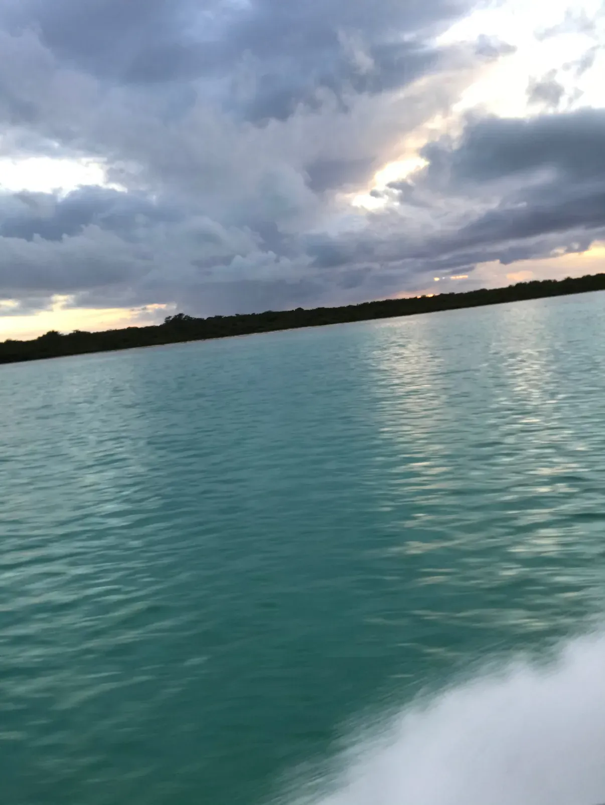 The boat's wake curling through still, teal water under a moody sky