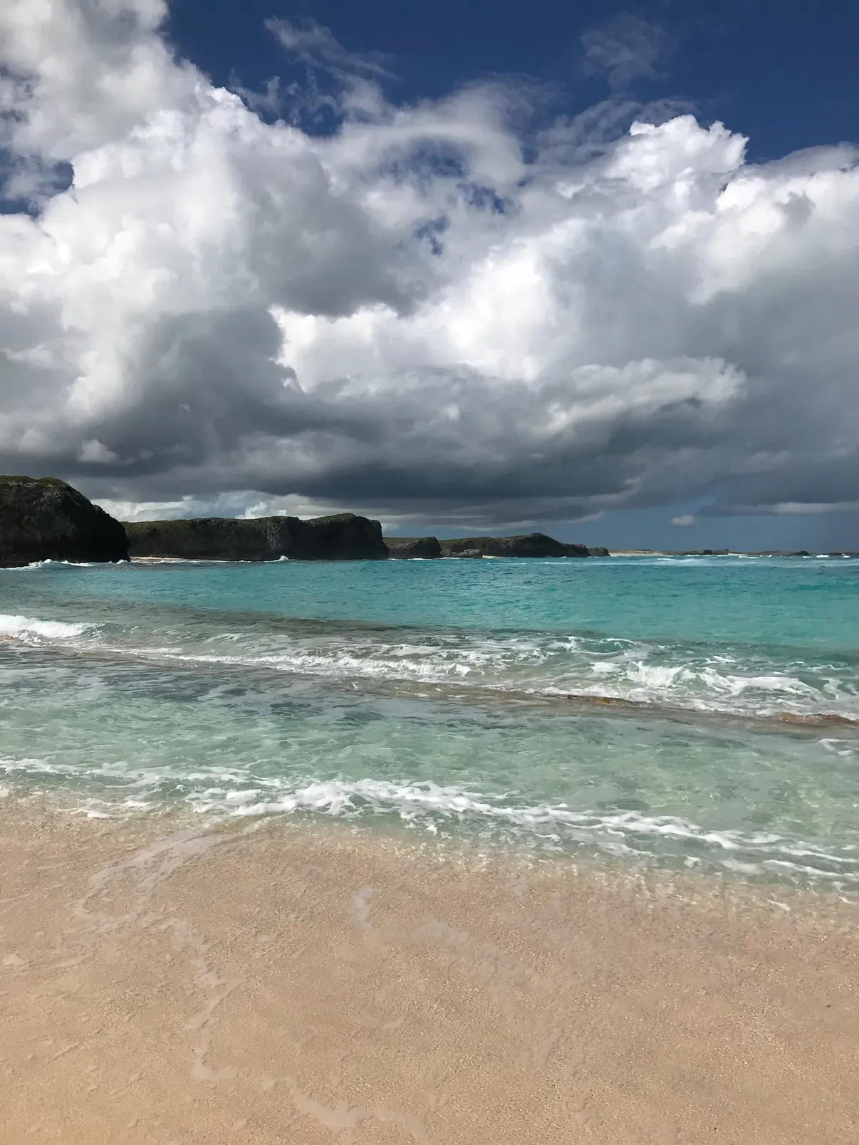 Surf breaking on an empty North Caicos beach under towering white cumulus clouds