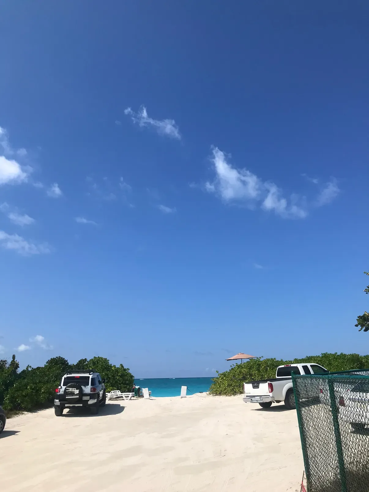 The road running down to a white-sand beach, rental cars parked at the end under a huge blue sky